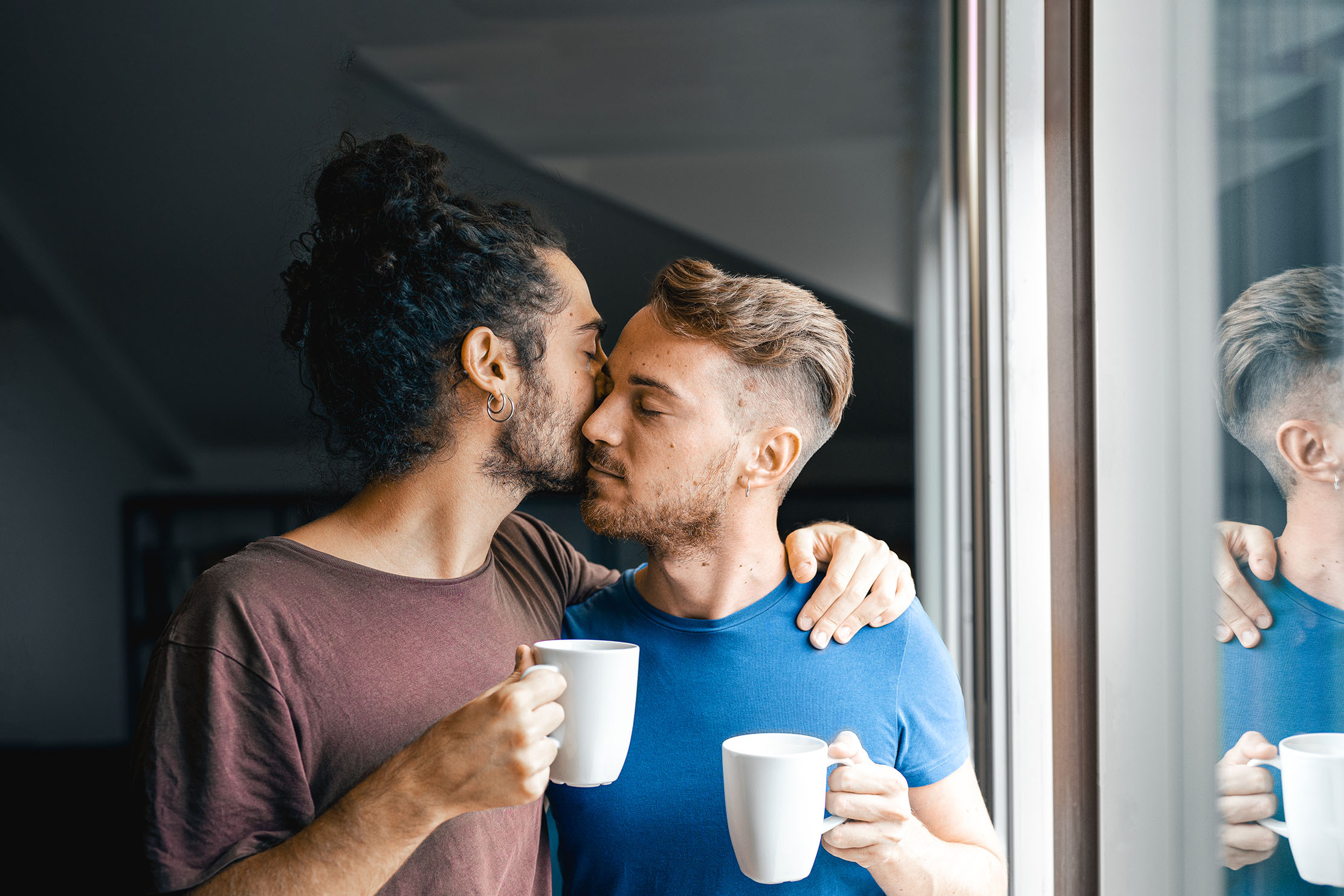 A couple enjoy a kiss on the cheek whilst holding mugs
